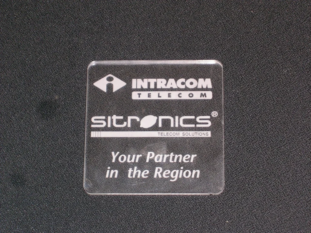 Κοπή και χάραξη laser σε διάφανο Plexiglass για την INTRACOM TELECOM, με λογότυπα INTRACOM και SITRONICS, στρογγυλεμένες γωνίες και λευκή σήμανση.